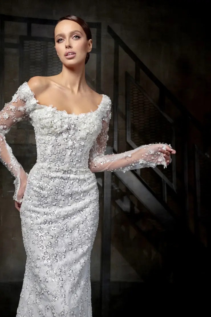 Model is wearing a sheath wedding dress with sheer illusion sleeves and a scoop neckline by autumn silk