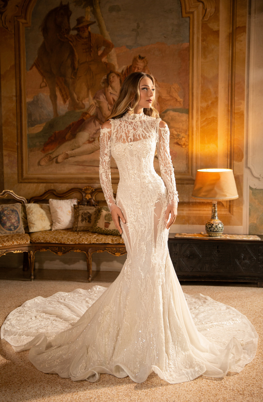 Model is wearing a cold-shoulder lace bridal gown with long sleeves and a high neckline in a fitted flare silhouette.