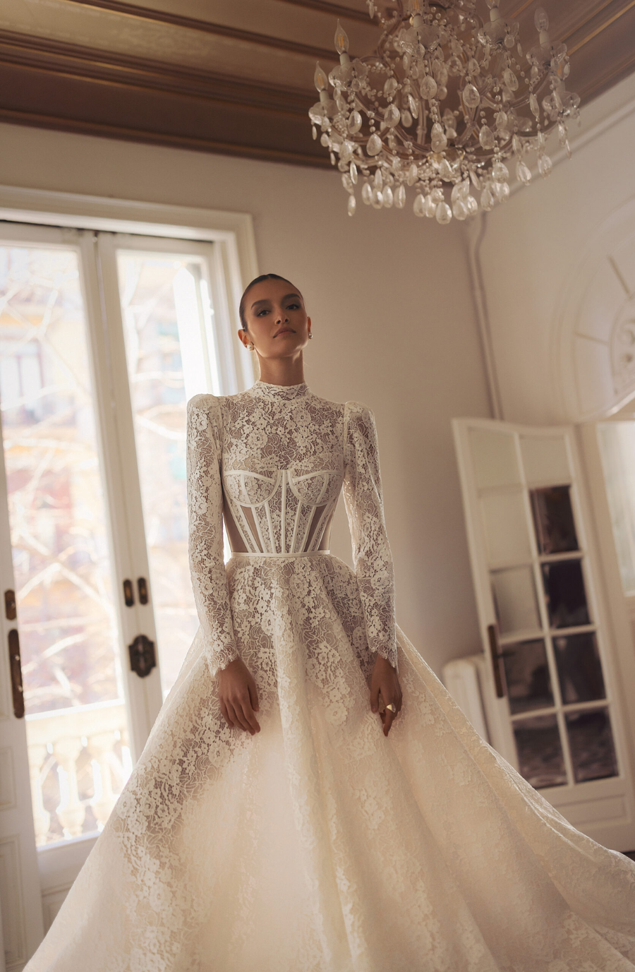 Model is wearing a long-sleeve lace wedding dress featuring a structured corset bodice.