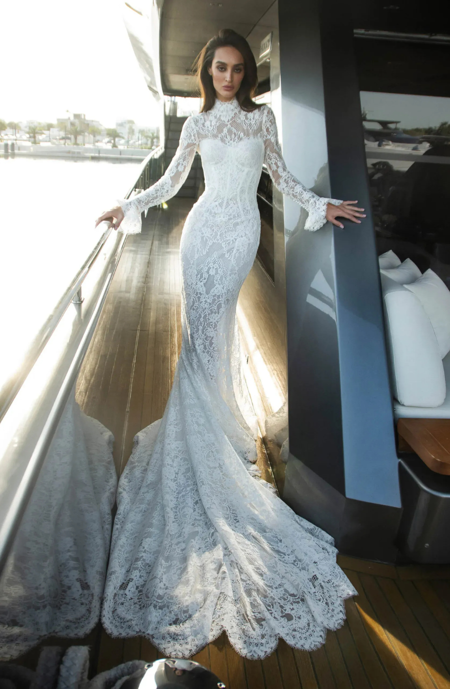 Model is wearing a long-sleeve lace bridal gown with a high neckline and an elegant extended train.