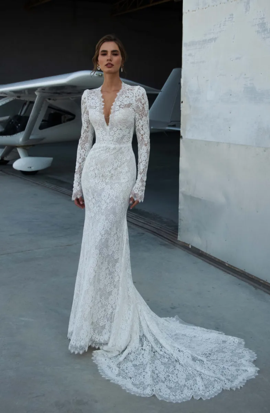 Model is wearing a long-sleeve lace fit-and-flare wedding gown with a graceful train.