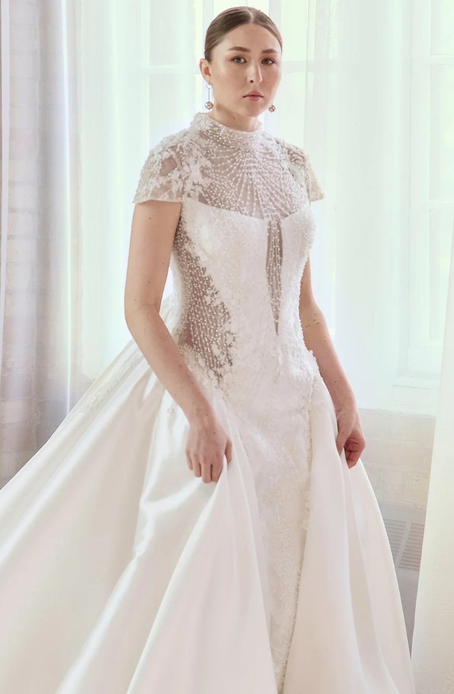 Model is wearing a modest high-neck dress with cap sleeves and a flowing overskirt.